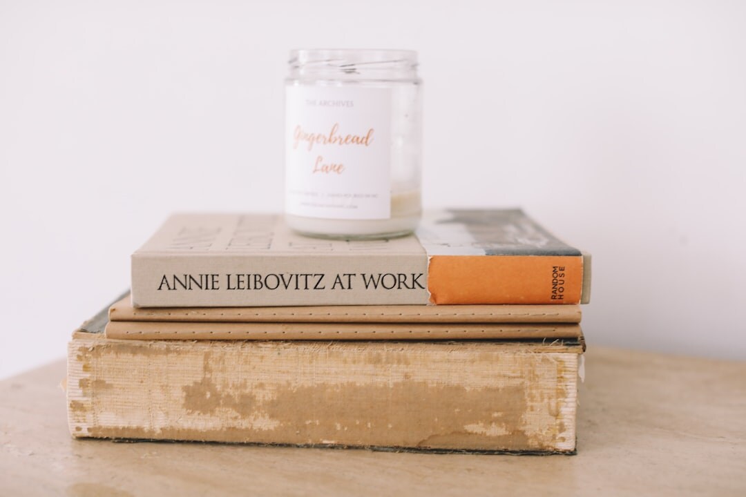 Stack of old hardcover mystery novels beside a lit candle on a dark wooden table
